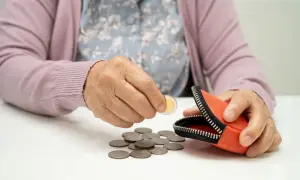 Dłoń starszej osoby wkłada monetę do portmonetki, obok leżą inne monety. Zastanawiamy się, ile wynosi najniższa renta z tytułu częściowej niezdolności do pracy.