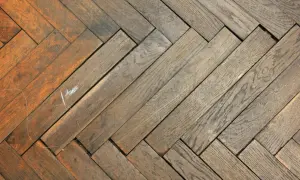 Abgenutztes Fischgrätparkett mit Kratzern und Verfärbungen, bereit für die Reparatur.