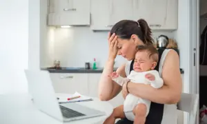 Zmęczona mama próbuje pracować przy laptopie, trzymając płaczącego, nadpobudliwego niemowlaka.