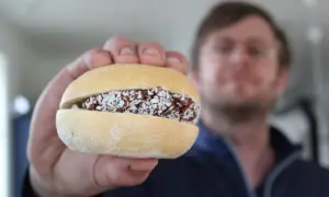 En hand håller upp en bulle med fyllning av choklad och kokosflingor. En man syns i bakgrunden. En riktig bulle med bulle!