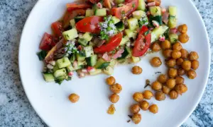 Salade colorée de tomates, concombres et pois chiches rôtis, garnie de petites fleurs blanches.