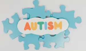 Niebieskie elementy układanki otaczają białą chmurkę z kolorowym napisem "AUTYZM". Psychiatra autyzm - wsparcie i zrozumienie.