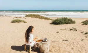 Kobieta pije herbatę na piaszczystych plażach Tunezji, z widokiem na ocean i falujące morze.