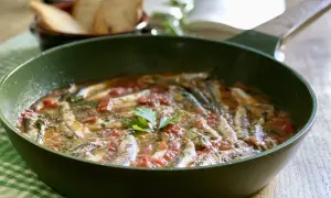 Un saporito bagnun di acciughe in padella, con pomodoro e prezzemolo, pronto per essere gustato con pane tostato.