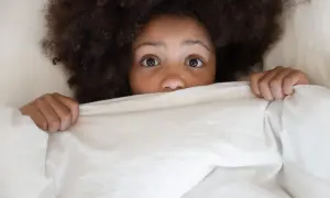Occhi sgranati di bambino nel letto, nascosto sotto le coperte, con un'espressione di pavor notturno.