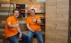 Dwóch mężczyzn w pomarańczowych koszulkach pokazuje kciuk w górę, gotowi pokazać, jak zbudować szafę.