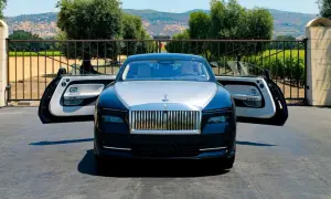 Elegancki Rolls-Royce Spectre z otwartymi drzwiami, zaparkowany przed bramą posiadłości z widokiem na wzgórza.