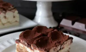 En bit krämig tiramisu, perfekt för ett tiramisu recept original. Pudrad med kakao, med kaffebönor och choklad i bakgrunden.