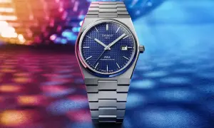 Reloj Tissot 1853 PRX Powermatic 80 con esfera azul texturizada y brazalete metálico, sobre un fondo vibrante de luces. Descubre su tissot 1853 precio.