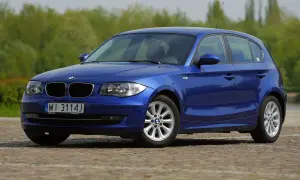 Niebieskie BMW E87 z polskimi tablicami WI 3114J, z nowymi żarówkami w reflektorach, zaparkowane na bruku.