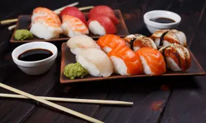 Jak wygląda sushi: na ciemnym drewnie ułożone są talerze z nigiri: krewetka, łosoś, biała ryba i węgorz. Obok sos sojowy i wasabi.