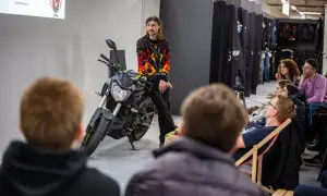 Mężczyzna w bluzie z płomieniami siedzi na motocyklu przed publicznością.