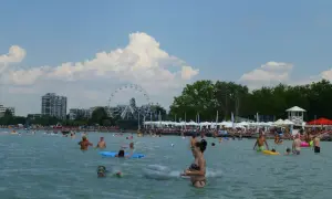 Ludzie kąpią się i relaksują na **Balaton plaża**. W tle widać diabelski młyn i budynki.