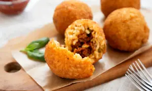 Arancini dorés et croustillants, une recette sicilienne à déguster. Un est un arancino ouvert révèle sa garniture savoureuse.