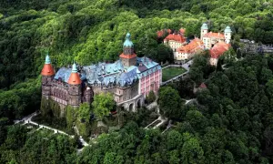 Zamek **Chudów** otoczony bujną zielenią, z charakterystycznymi wieżami i czerwonymi dachami, wygląda jak z bajki.
