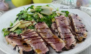 Deliziosa tagliata di tonno scottata, cosparsa di semi di sesamo nero, servita con un'insalata fresca di rucola e scaglie di parmigiano.