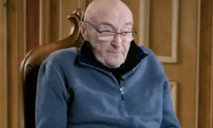 Phil Collins w okularach, siedzi w fotelu. Jego choroba wpływa na jego zdolność do gry na perkusji, ale nadal inspiruje fanów.