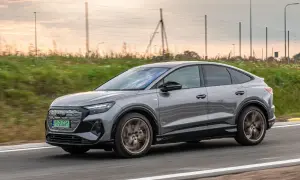 Szary Audi Q4 Sportback sunie po drodze, otoczony zielenią i zachodzącym słońcem.