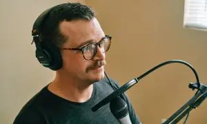 Mężczyzna w słuchawkach i okularach z wąsami ustawia mikrofon.