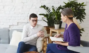 Mężczyzna w okularach rozmawia z kobietą, która notuje. To typowa scena, gdy psychoterapeuta pomaga pacjentowi.