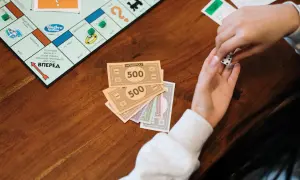 Ręce trzymają kości i pieniądze z gry Monopoly. Naucz się, jak rozdawać pieniądze w Eurobiznes, by wygrać!