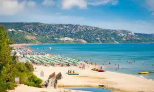 Słoneczna plaża z mnóstwem leżaków i parasoli, ludzie kąpią się w morzu. To idealne miejsce na wakacyjne atrakcje w Grecji.