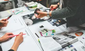Manos trabajando en un proyecto de marketing internacional, recortando imágenes y escribiendo ideas en hojas de papel.