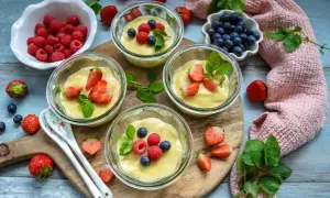 Vier Gläschen cremiger Vanillepudding, garniert mit frischen Erdbeeren, Himbeeren und Blaubeeren. Ein süßer Genuss!