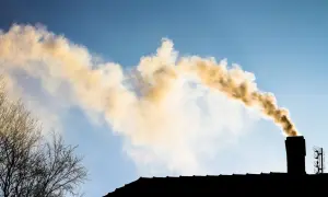 Dym z komina, który mógłby świadczyć o tym, że zakaz palenia węglem uchylony. Widać też sylwetkę dachu i drzew.