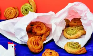 Zwei weiße Papiertüten quellen über mit köstlichen Pesto-Schnecken. Einige sind goldbraun, andere mit grünem Pesto gefüllt.