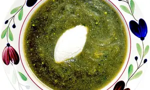 A bowl of green soup with a dollop of cream, garnished with colorful floral patterns.