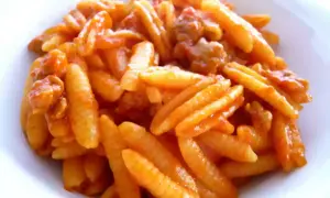 Malloreddus alla campidanese, pasta sarda con sugo di pomodoro e salsiccia, un piatto ricco e saporito.