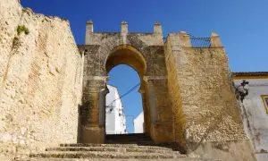 Antigua puerta de acceso a Medina Sidonia, con escalinata de piedra y cielo azul. Merece la pena visitar Medina Sidonia.