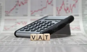 Kalkulator i kostki z literami VAT na tle wykresów finansowych. Pełna księgowość krok po kroku.