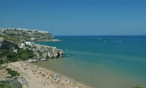 Peschici spiaggia Zaiana, con gente che prende il sole e nuota nelle acque cristalline sotto un cielo azzurro.