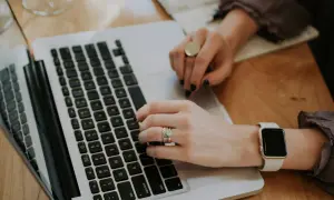 Kobieta pisze na laptopie, analizując odsetki ustawowe. Na palcach ma obrączkę i pierścionek, a na nadgarstku smartwatch.