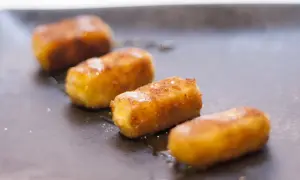 Friterad fetaost i stavar, gyllene och krispiga, serverade på en mörk tallrik med en lätt glasyr.