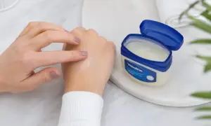 Dłoń rozsmarowuje wazelinę, sprawdzając, czy wazelina nawilża. Słoiczek Vaseline stoi obok.