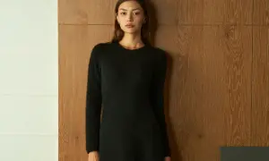 Frau in schwarzem Strickkleid vor Holzvertäfelung. Ein schlichtes Outfit, das zu den modernen Dresscodes für Frauen passt.