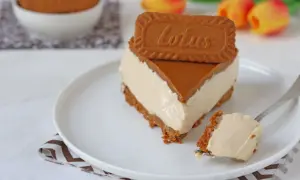 Una fetta di cheesecake Lotus, con biscotto e caramello, su un piatto bianco. Un morso su una forchetta.