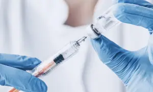 Ręce w niebieskich rękawiczkach pobierają płyn z fiolki do strzykawki. To może być propofol, środek znieczulający.