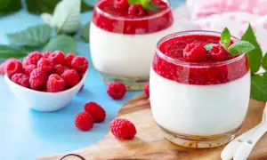Deux panna cotta framboise, garnies de fruits rouges frais et de menthe, sur un plateau en bois.