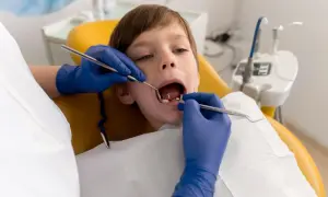 Chłopiec przechodzi leczenie amputacyjne zębów mlecznych. Dentysta w niebieskich rękawiczkach bada jego ząbki.