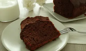 Fette di plumcake al cioccolato su un piatto, con una forchetta e un bicchiere di latte sullo sfondo.