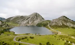 Paisaje montañoso con un lago sereno y carreteras sinuosas. Se puede ver gente disfrutando del **subir Lagos de Covadonga**.