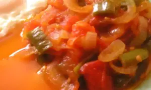 Une assiette de piperade recette, avec des poivrons verts, des oignons et des tomates mijotés, à côté d'un œuf au plat.