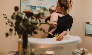 Mamma håller sitt barn redo för att bada. En leksak i form av en giraff ligger i badkaret.