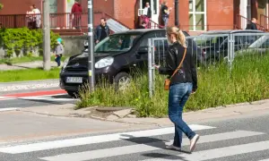 Młoda kobieta, pieszy, idzie przez pasy, patrząc w telefon.