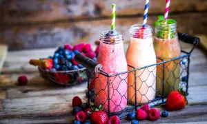 Drei bunte Flaschen mit leckeren Smoothies zum Abnehmen, umgeben von frischen Beeren und Erdbeeren auf rustikalem Holz.