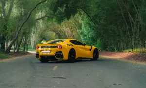 Żółte Ferrari F12 TDF sunie po leśnej drodze, otoczone bujną zielenią.
